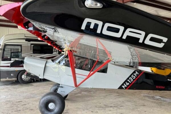 A low angle view of the N413SM aircraft showing the underside of the wing and the MOAC logo.