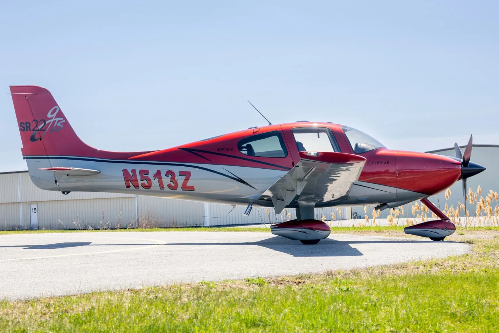 A red and grey Cirrus SR22T aircraft (N513Z) parked on an asphalt runway, side view.