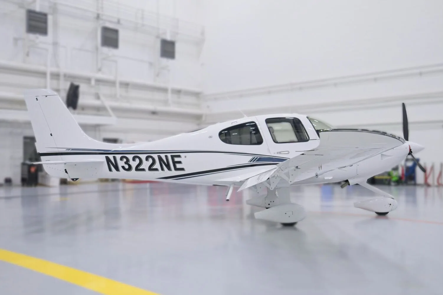 A side view of a white Cirrus SR22 aircraft with black and blue stripes, N322NE, in a hangar.