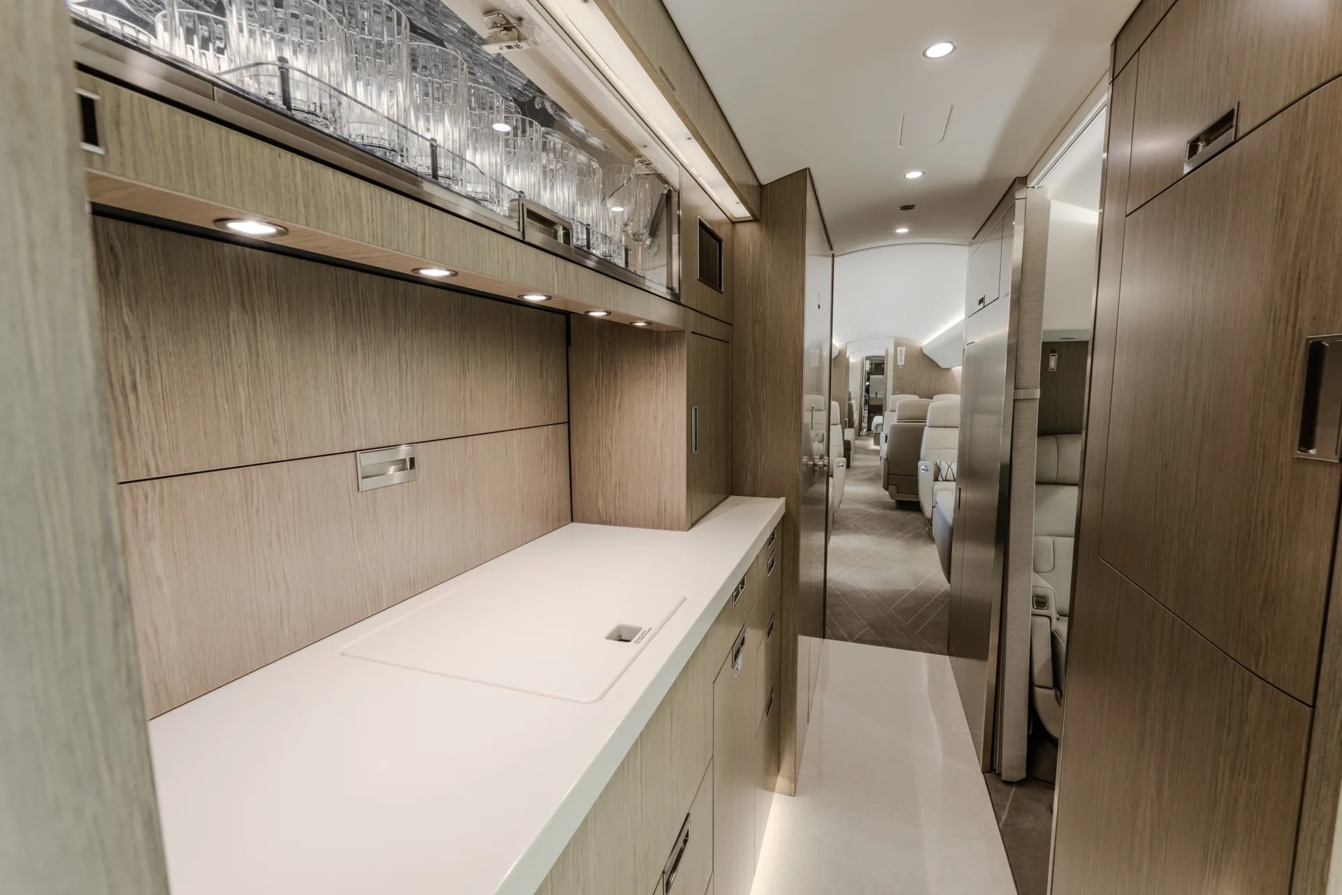 A view of a private jet's galley area with wooden cabinetry, a white countertop, and glassware storage.