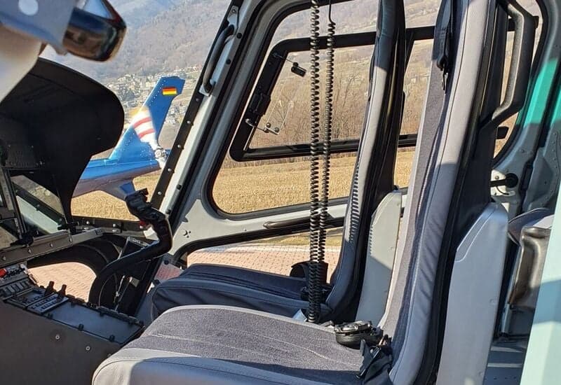 The interior of a helicopter with gray seats and a view of the tail of another aircraft.