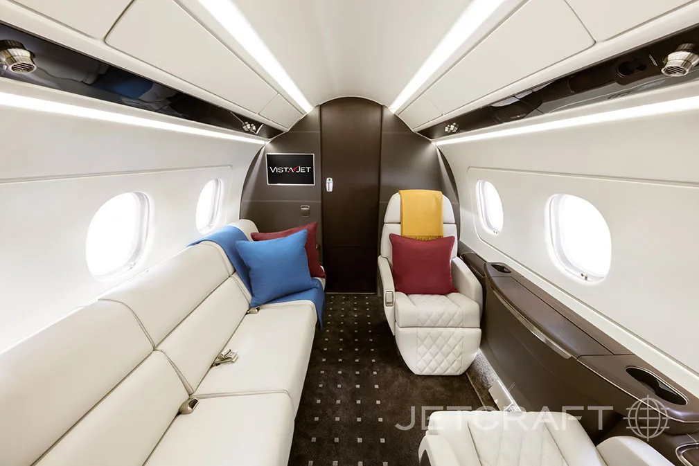 The interior of a jet aircraft with white leather seats and a sofa.