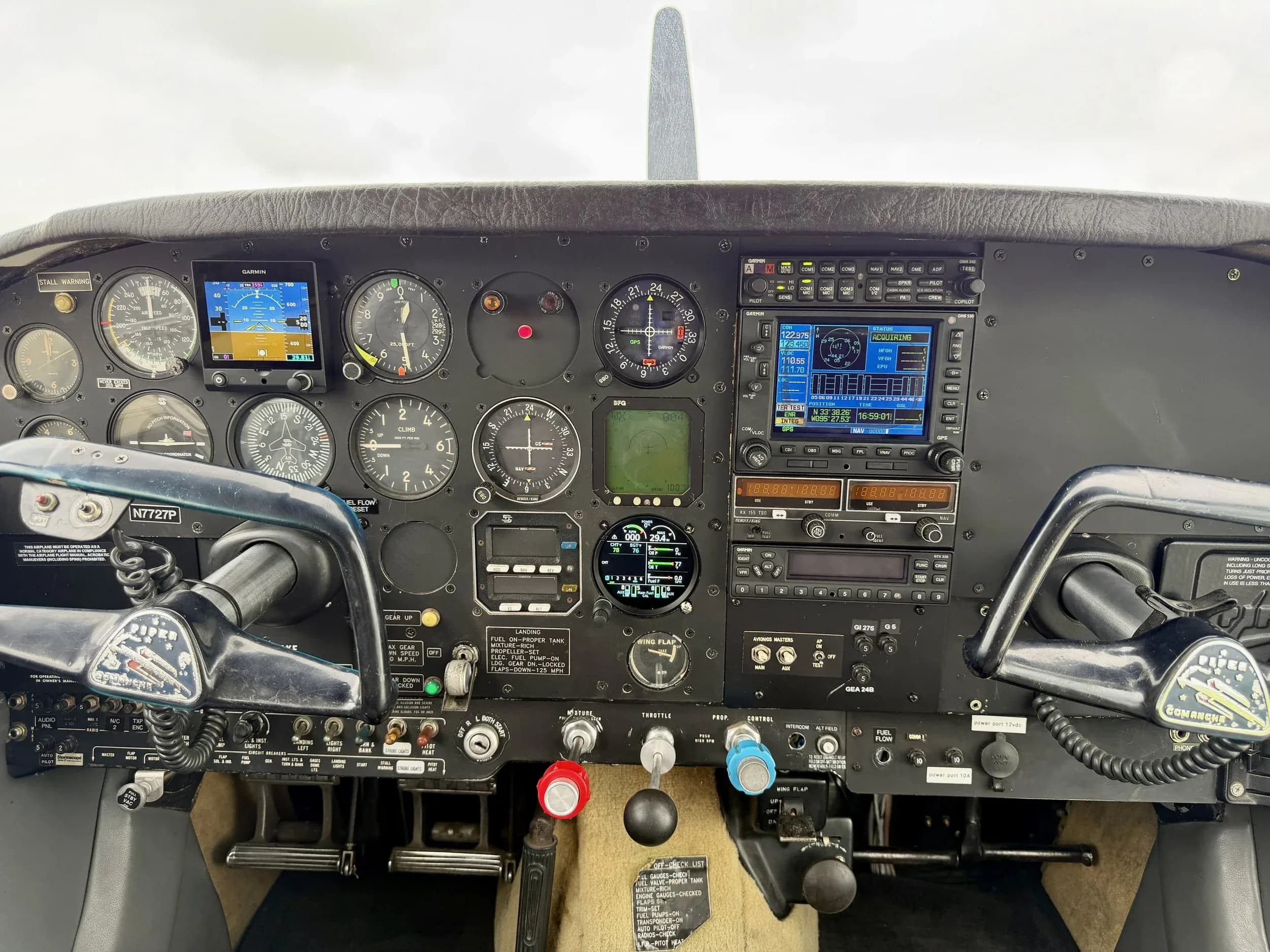The cockpit of a Piper Comanche N7727P with various analog gauges and modern digital displays.