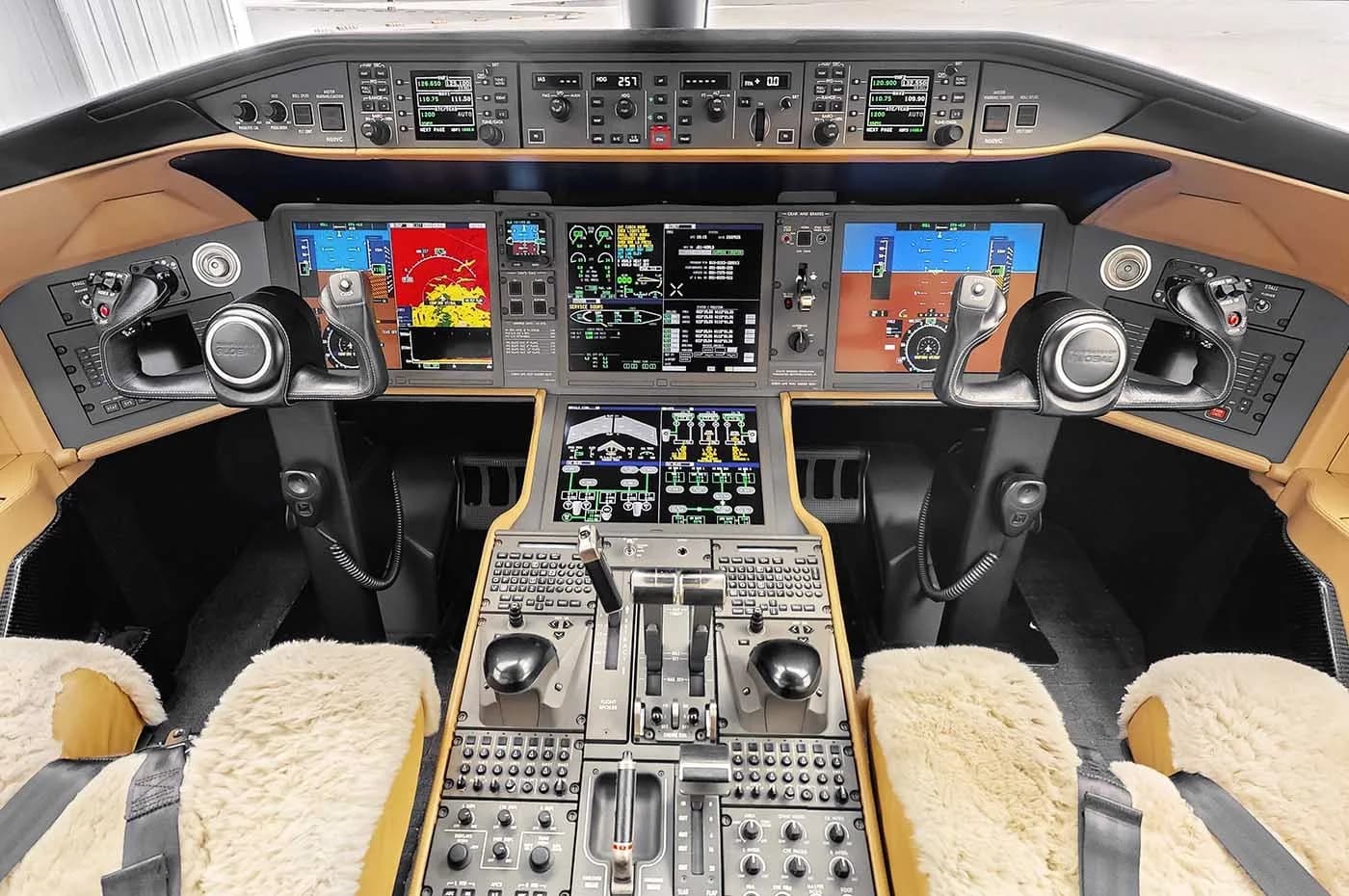 The modern cockpit of a business jet, featuring multiple digital displays, control yokes, and sheepskin seat covers.