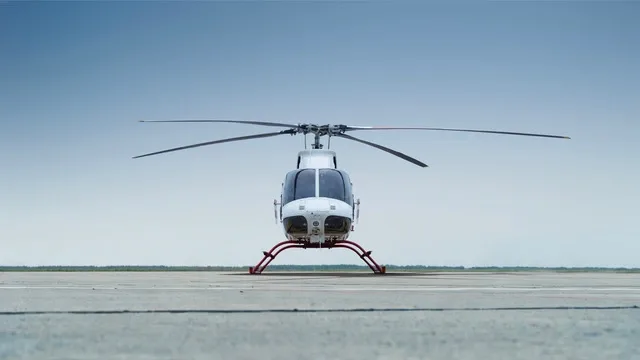 A white and red Bell 505 helicopter is shown from the front, parked on an airfield.