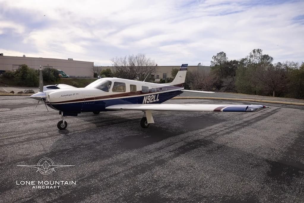 A three-quarter front view of the Piper Saratoga II TC aircraft (N92LL) with blue and white paint scheme parked on an asphalt apron.