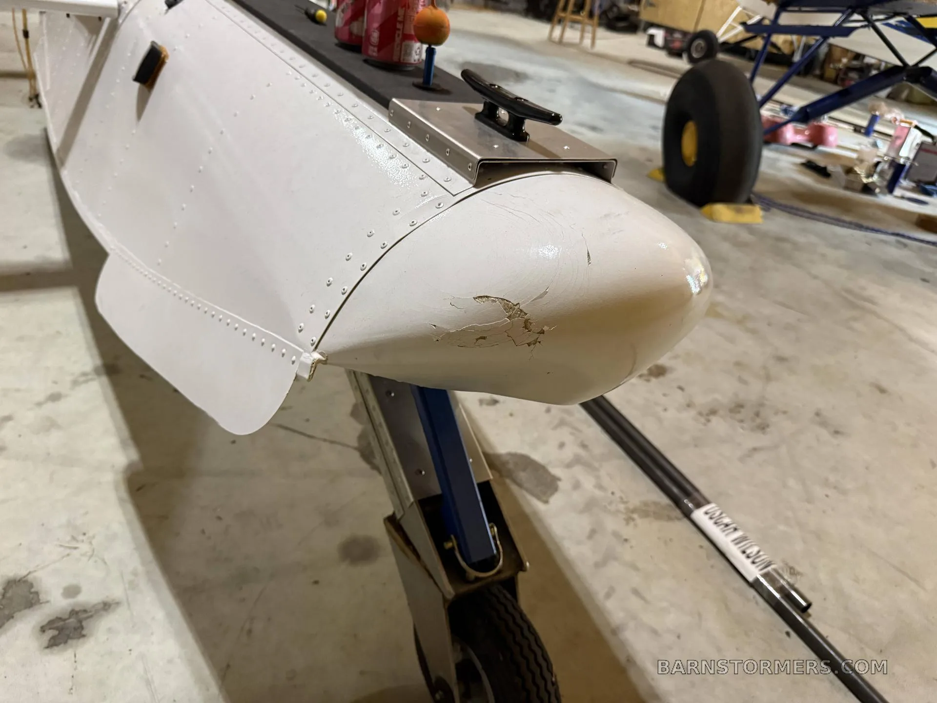 A close-up view of the front of a white aircraft float with some paint chipping, showing its wheel and strut.