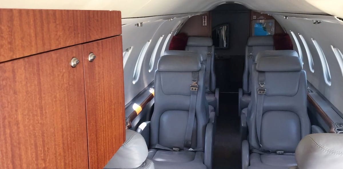 Aircraft cabin with gray leather seats and wood cabinetry.