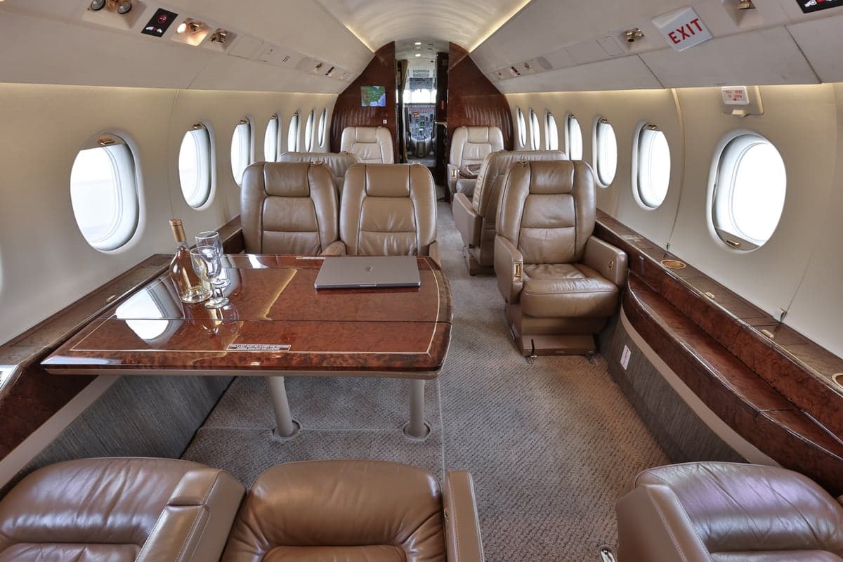 View of the aircraft interior with leather seats and a table with a laptop and wine.