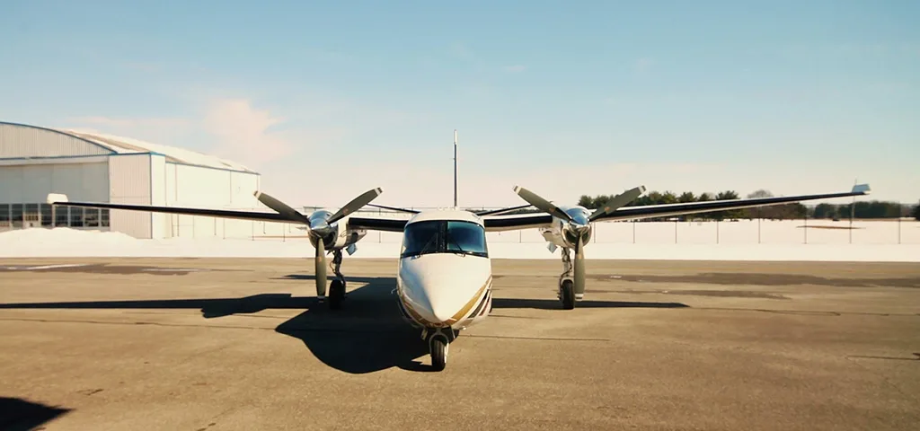 A head-on view of a white twin-engine turboprop aircraft with gold and maroon stripes parked on an airfield.