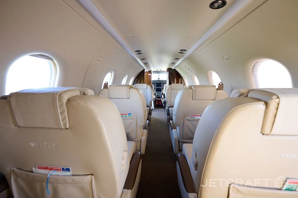 A view down the aisle of the aircraft cabin, showing rows of light cream leather seats.