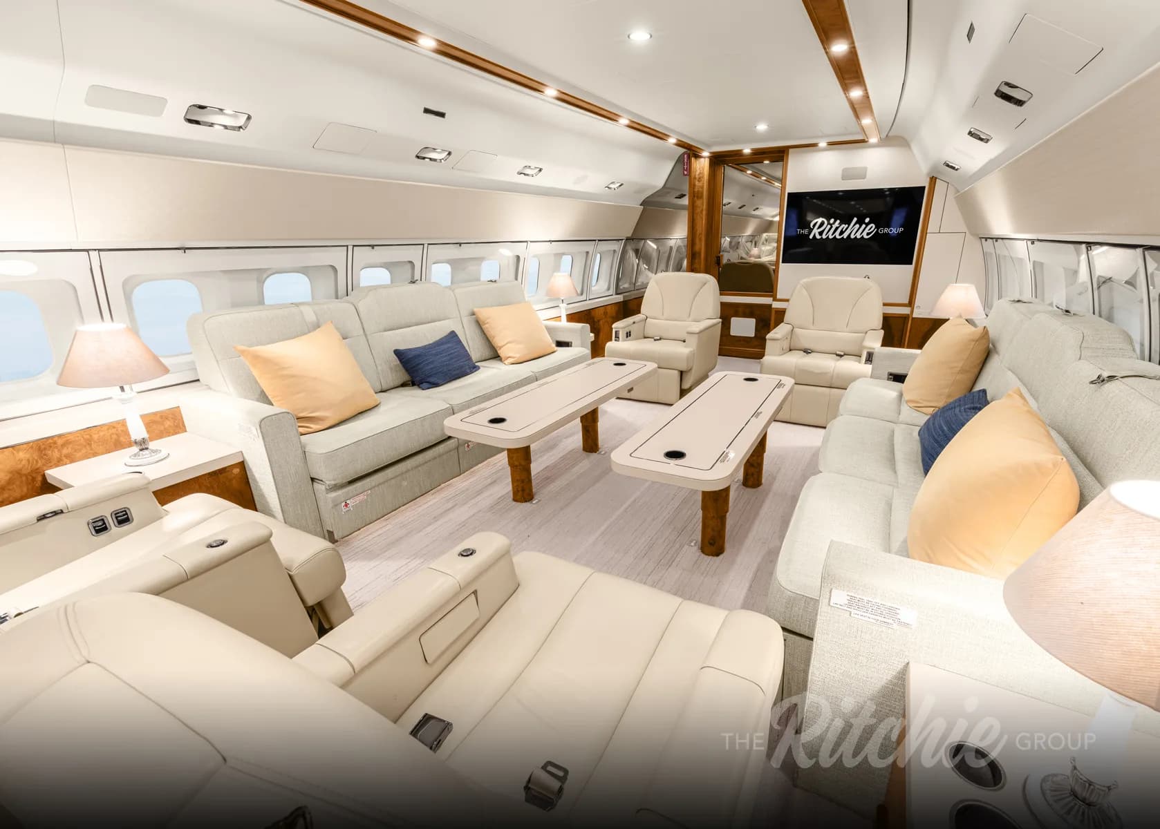 A luxurious aircraft cabin with light-colored sofas, chairs, and wooden tables.