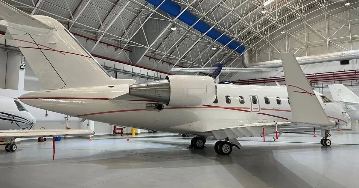 A white business jet with red pinstripes parked inside a hangar, viewed from the rear-right.