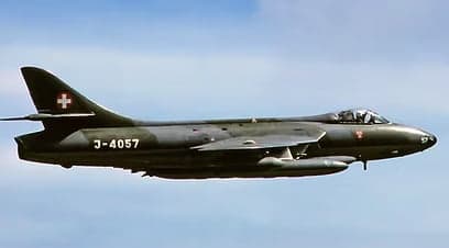 A Swiss Air Force Hawker Hunter, registration J-4057, in flight against a blue sky.