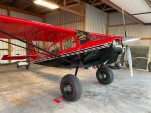 A red and black Cubcrafters aircraft is parked inside a hangar.