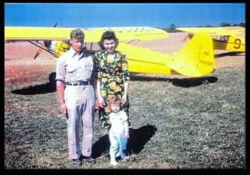 A family stands in front of a yellow Piper Cub aircraft.