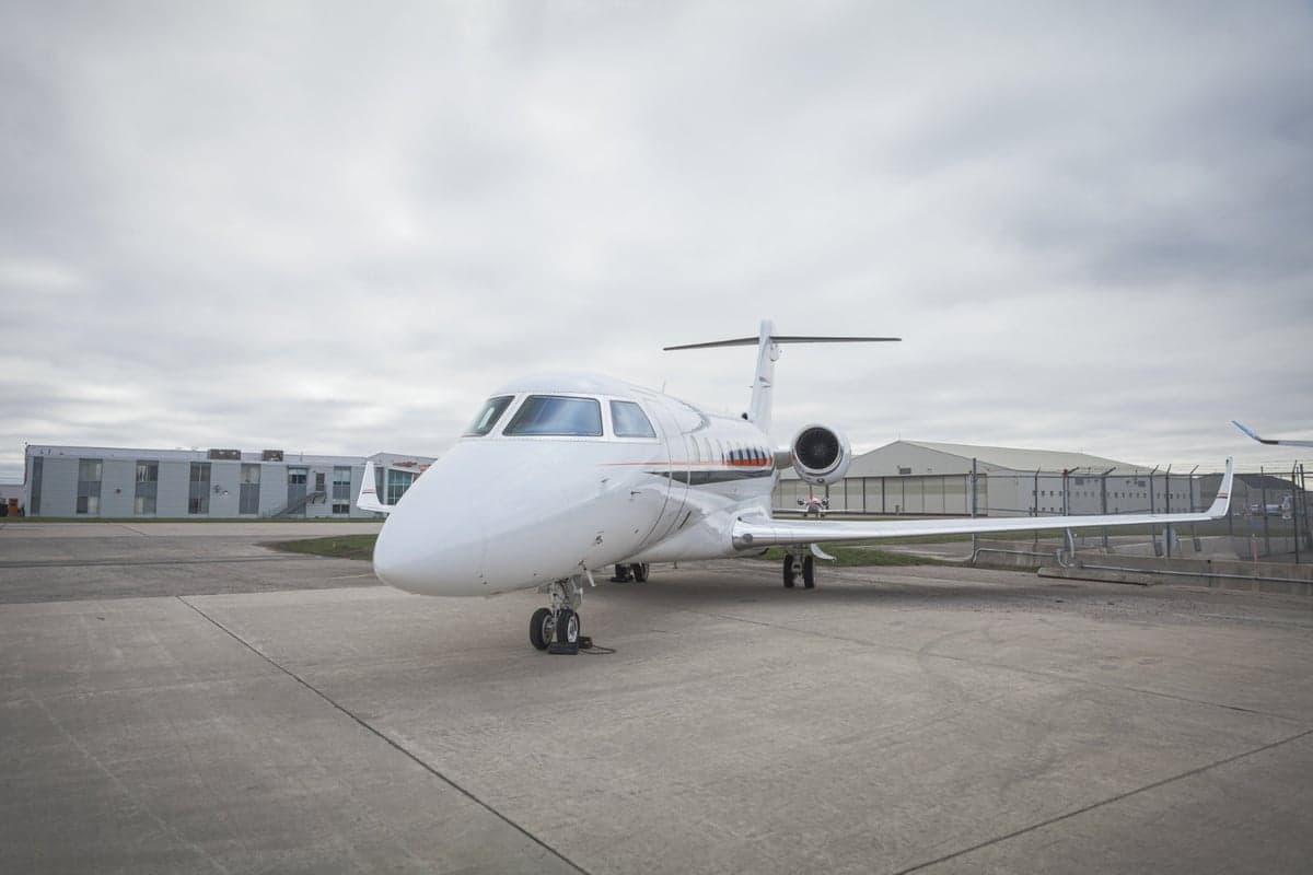 A white private jet is parked on the tarmac under a cloudy sky.