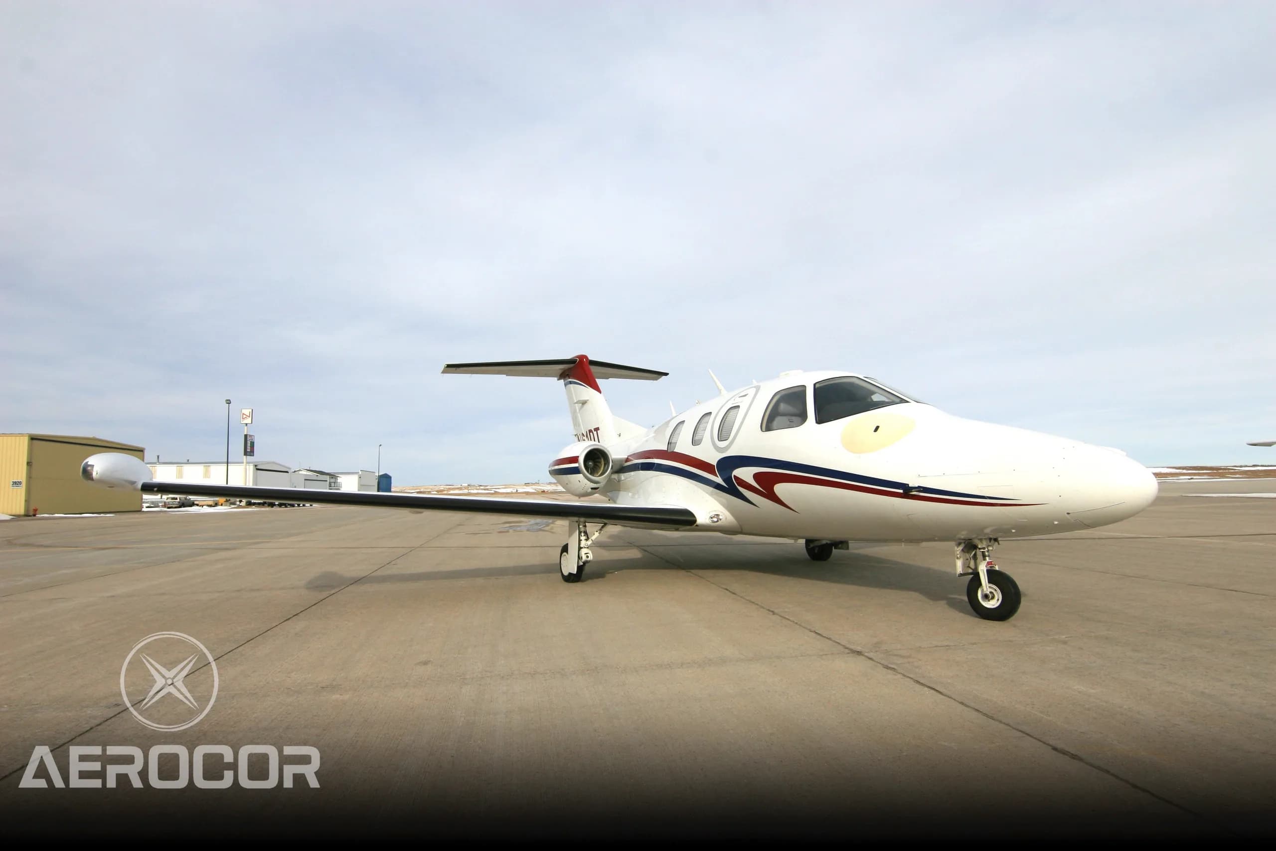 A white Eclipse 500 jet with red and blue stripes parked on an airport tarmac, viewed from the front.