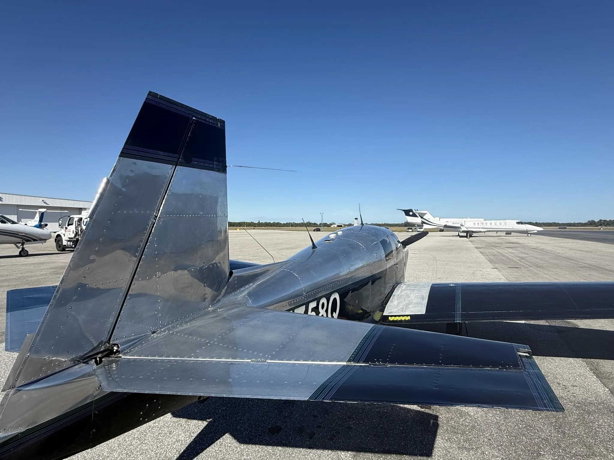 Rear-side view of a black and silver Mooney M20 aircraft, N5758Q, parked on an airfield with other aircraft.