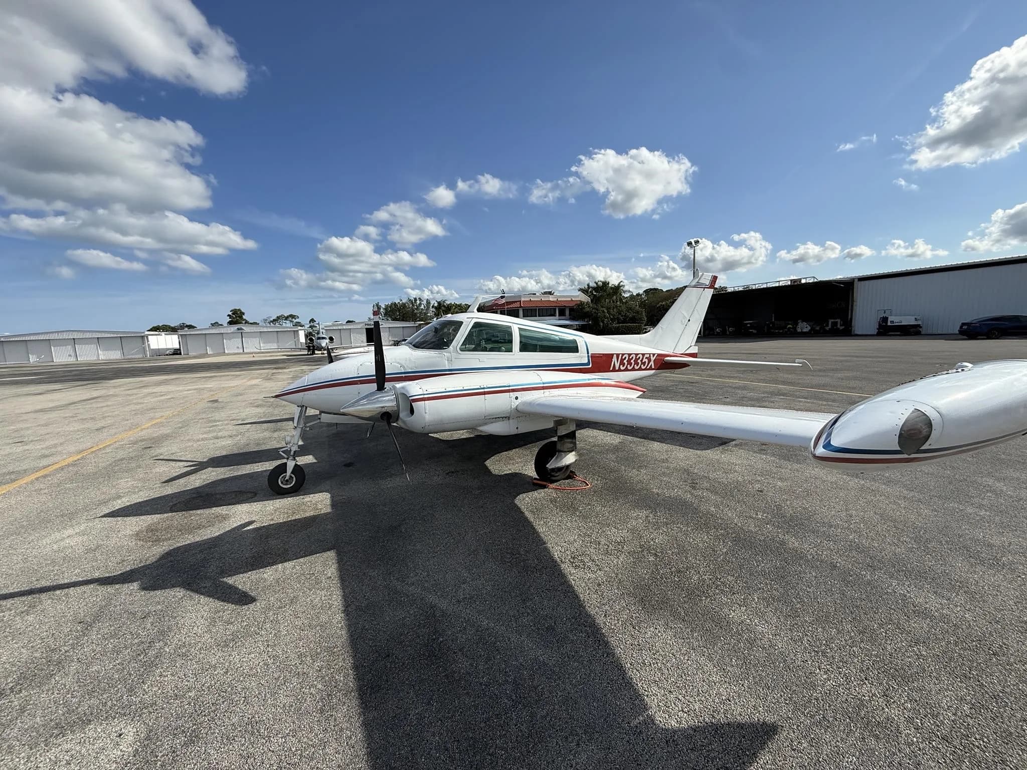 A white Cessna 310L with red and blue stripes parked on an airport tarmac, showing the left side.