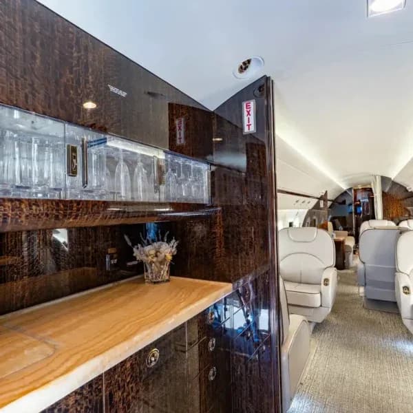 A close-up of the aircraft's galley or bar area with a light-colored countertop, glassware storage, and dark wood paneling.