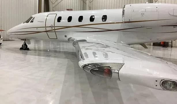 A close-up view of the front fuselage and wing of a white Cessna Citation business jet with gold and brown stripes, parked in a hangar.