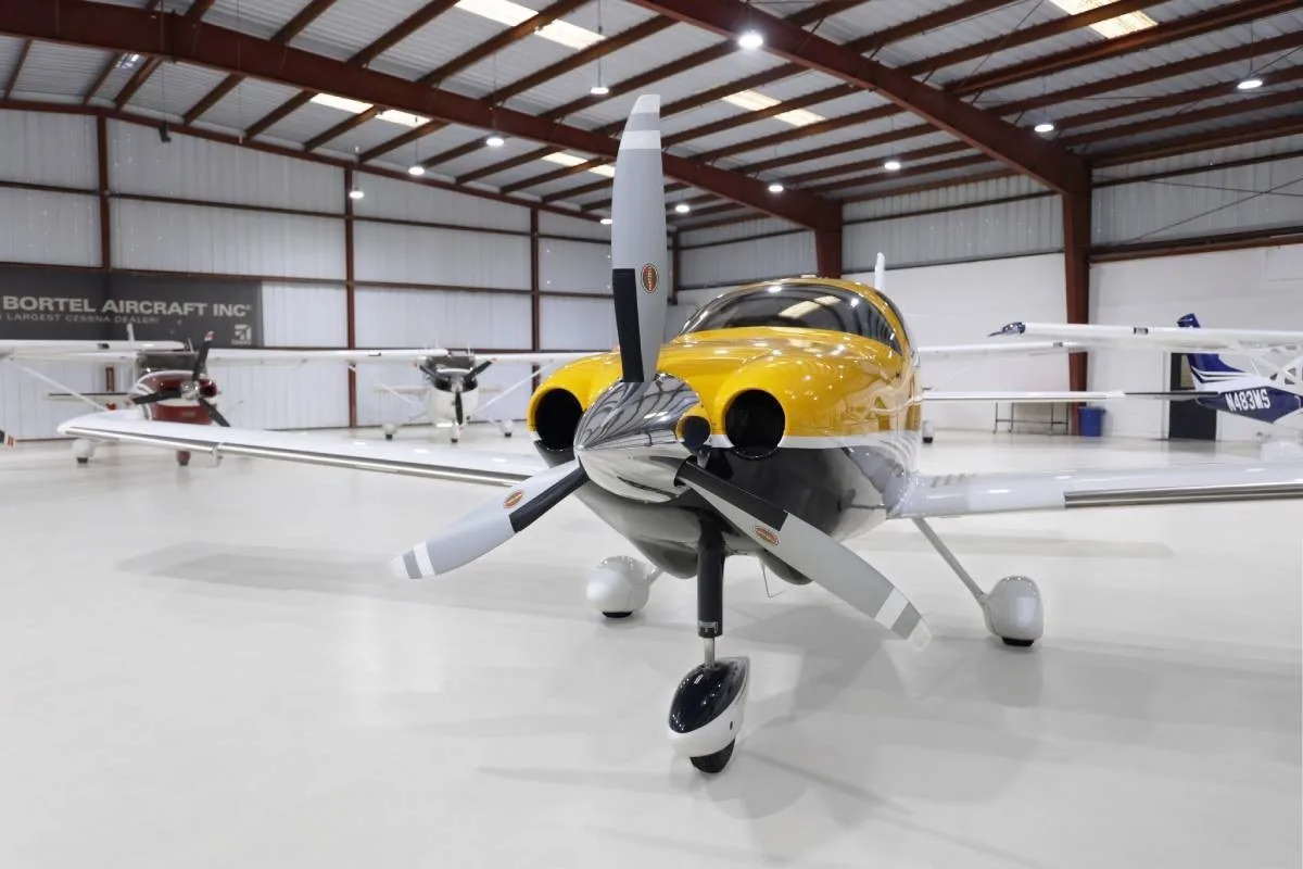 A head-on view of the yellow and white Cessna TTx (N105RG) with its propeller, parked in a hangar.