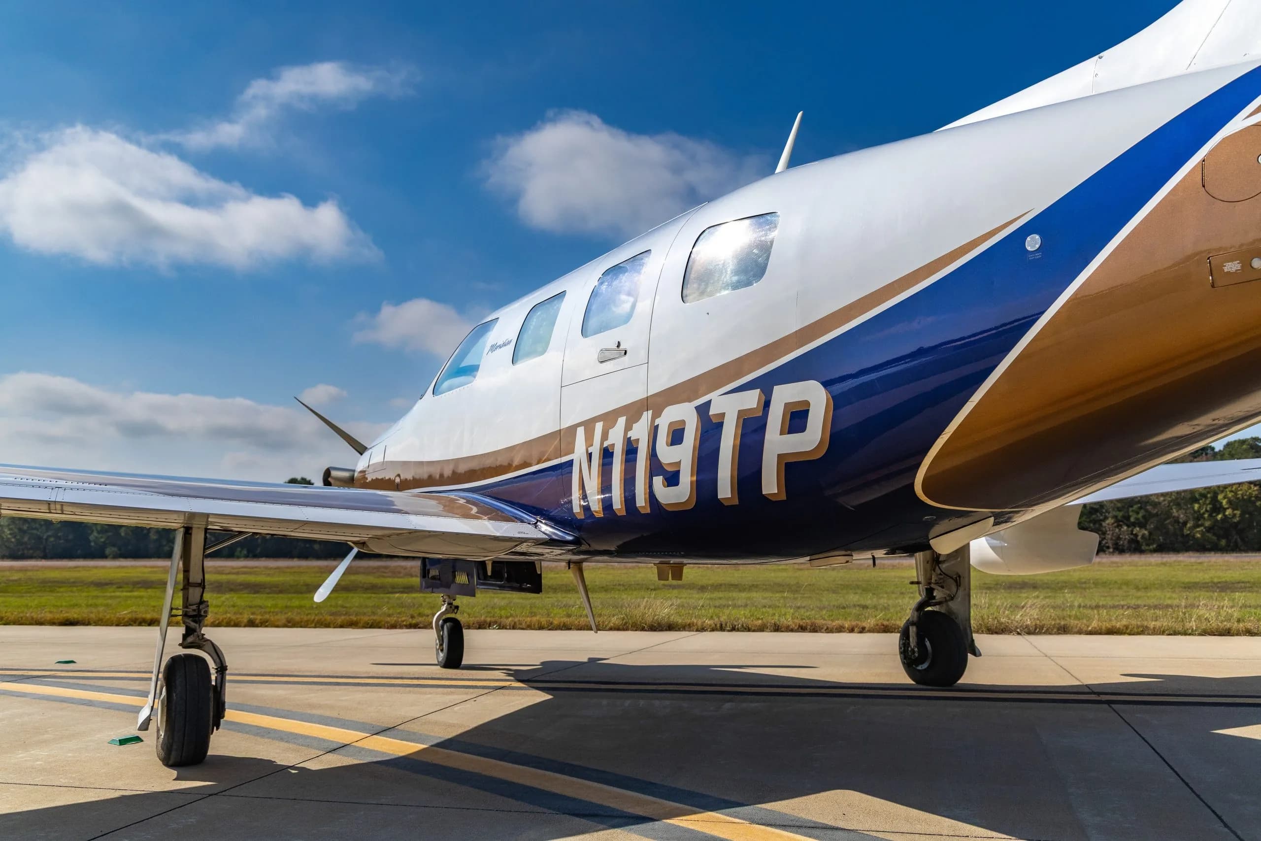 A close-up of a white and blue Piper Meridian aircraft, registration N119TP, showing the fuselage and wing.