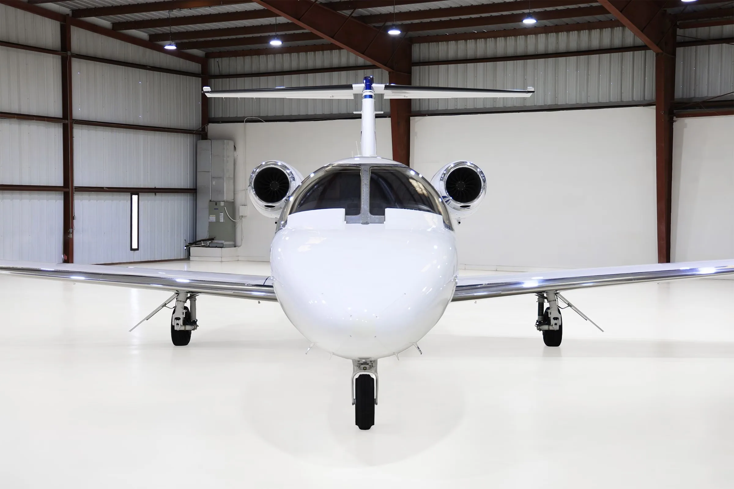 A head-on view of a white Cessna Citation CJ2+ (N525WD) with blue stripes parked in a hangar.