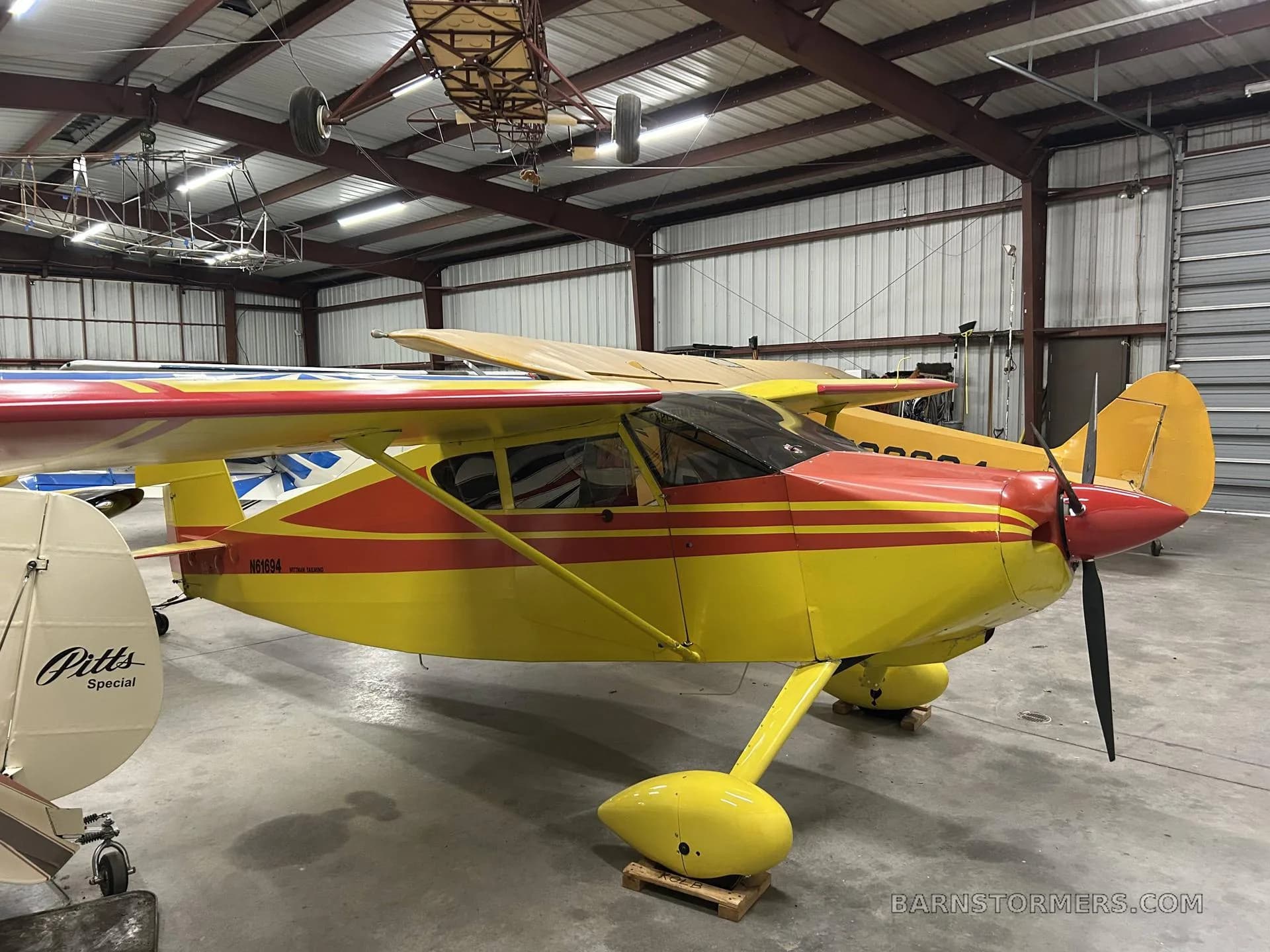 A yellow and red single-engine aircraft with tail number N61694 is parked in a hangar.