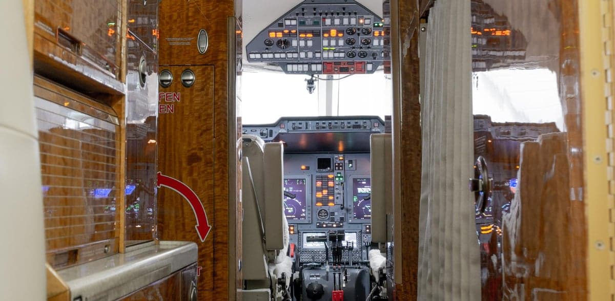 A view from the aircraft cabin looking into the illuminated cockpit with wood paneling.