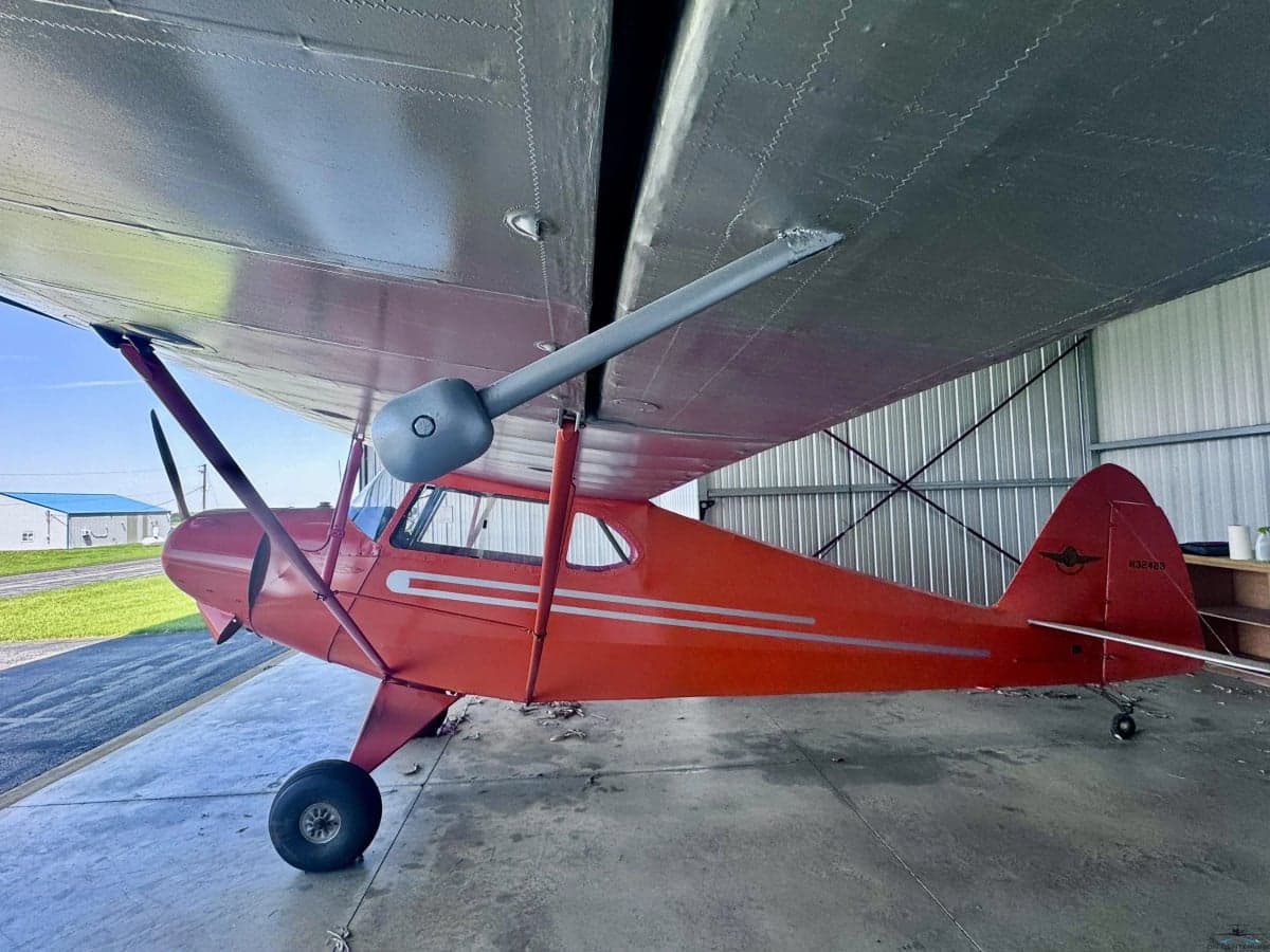 A side view of the orange vintage aircraft with registration N32428, parked in a hangar.