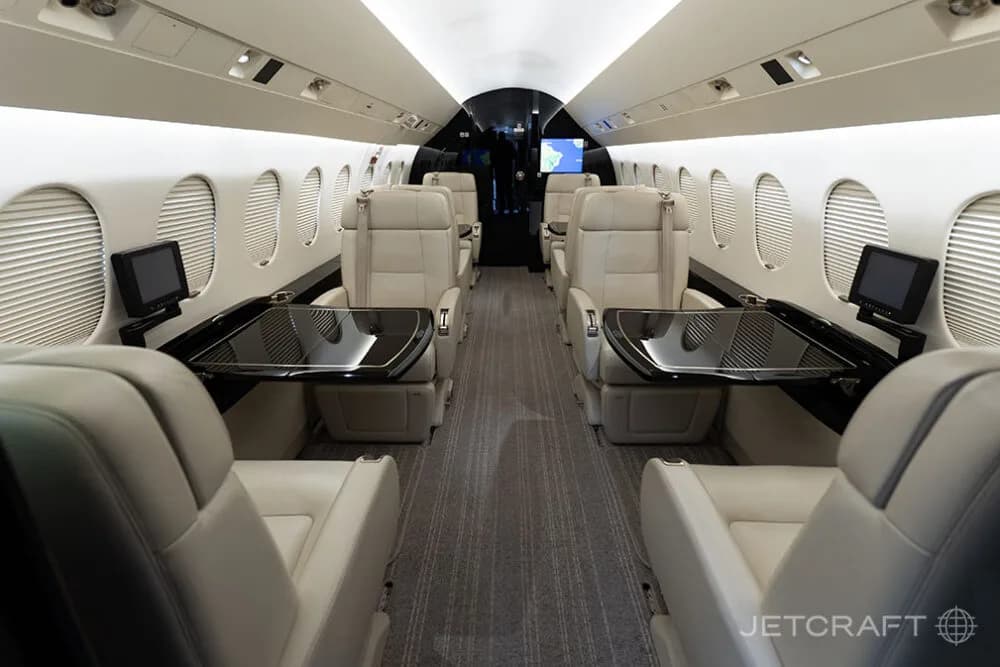 The luxurious cabin interior of a business jet with beige leather seats and dark tables.
