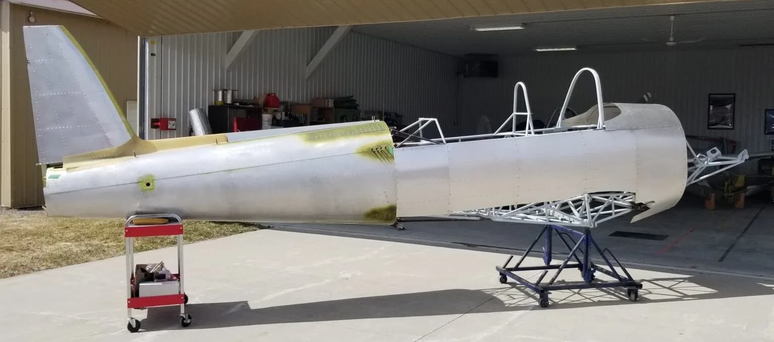 A partially assembled aircraft fuselage, with the tail section attached, sitting on stands outside a hangar.