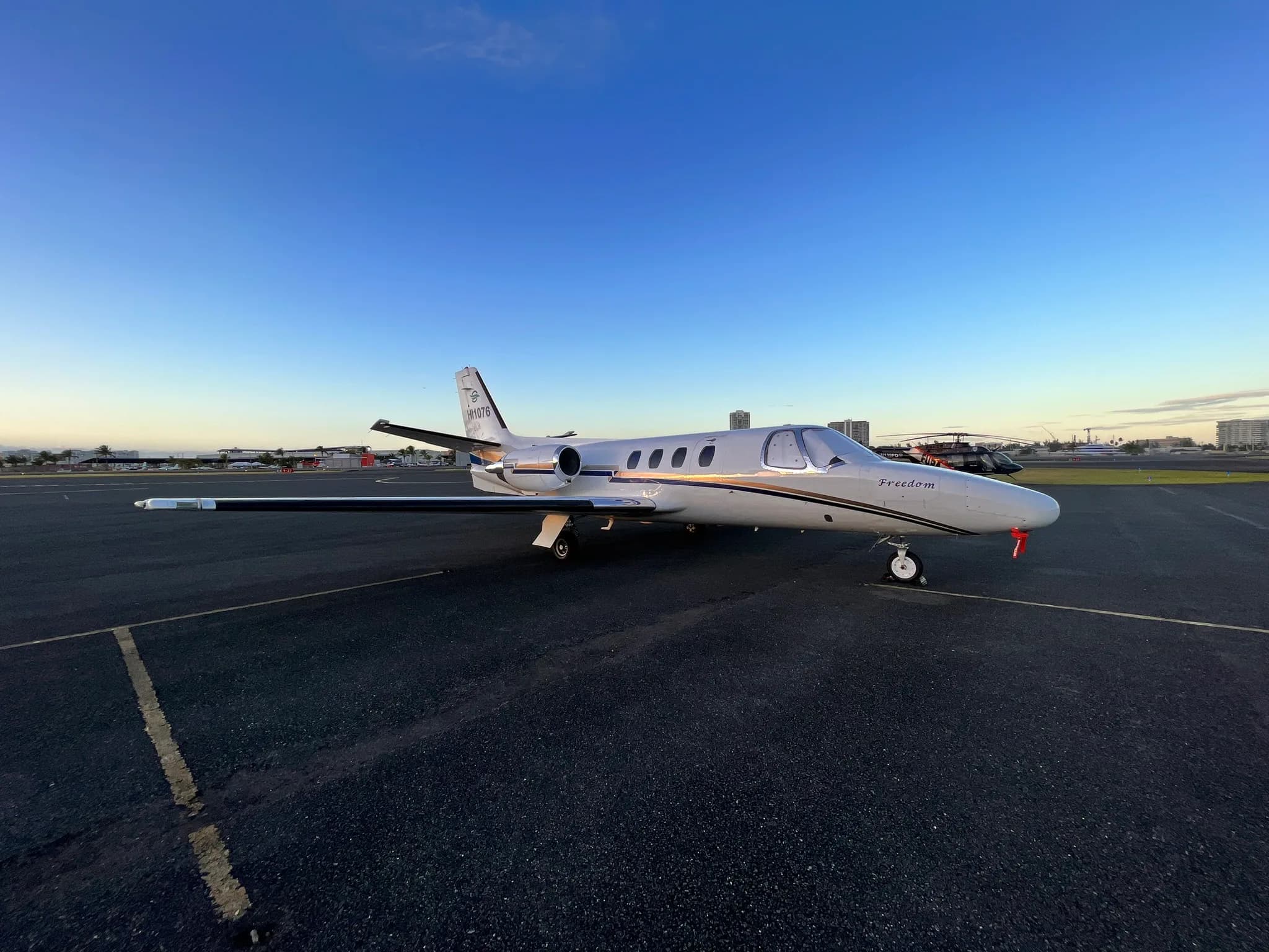 Side view of a white Cessna Citation Mustang with black and gold stripes on the tarmac.