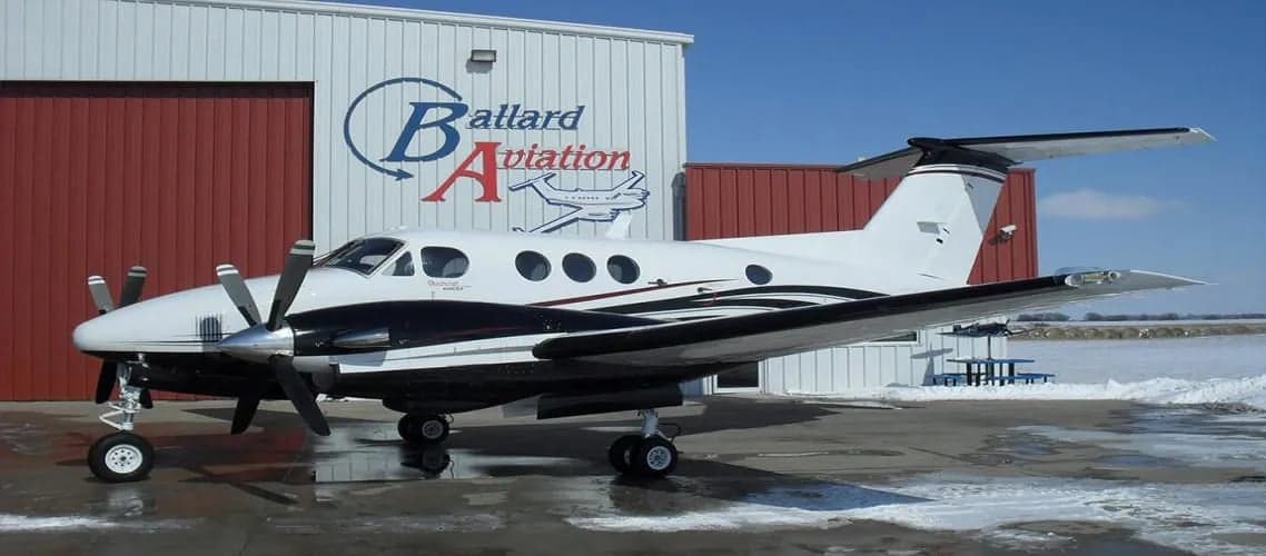 A King Air turboprop aircraft parked in front of a hangar.