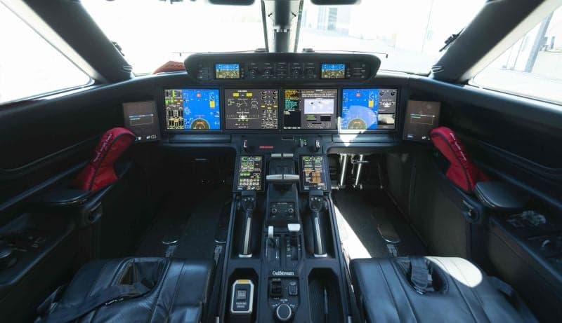 The aircraft's interior features a sofa, cream-colored leather seats, and wood accents.