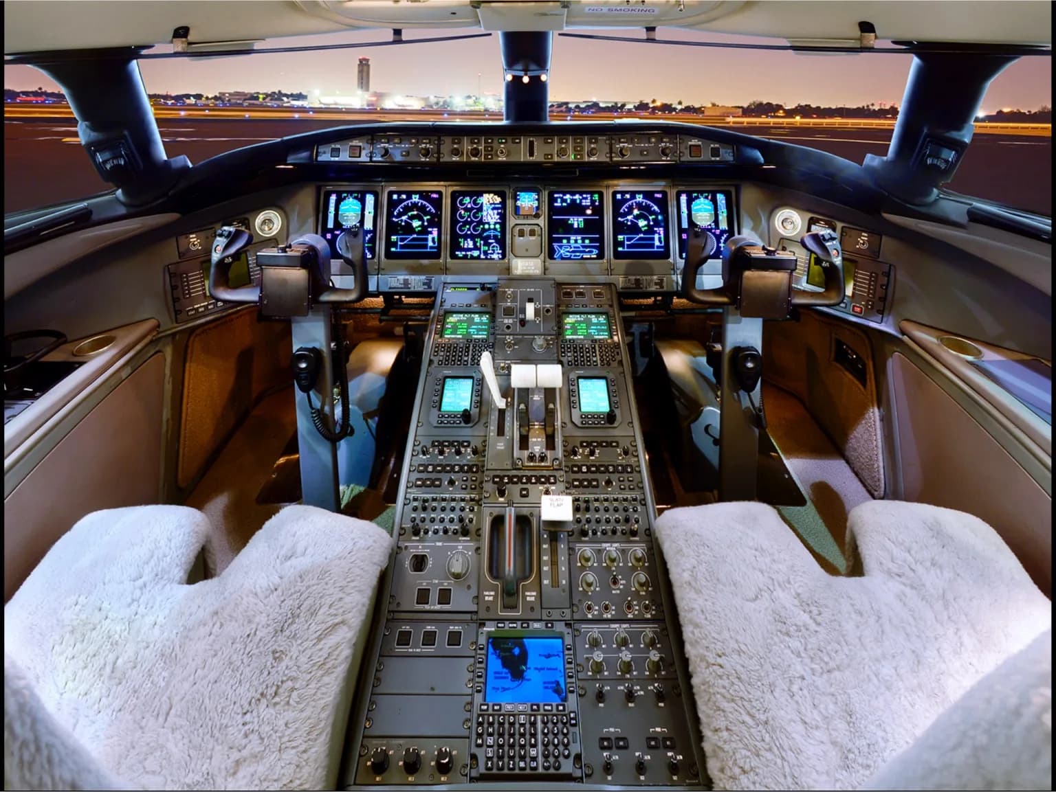 The cockpit of a private jet with multiple digital displays and controls, seen from the pilot's seat at night.