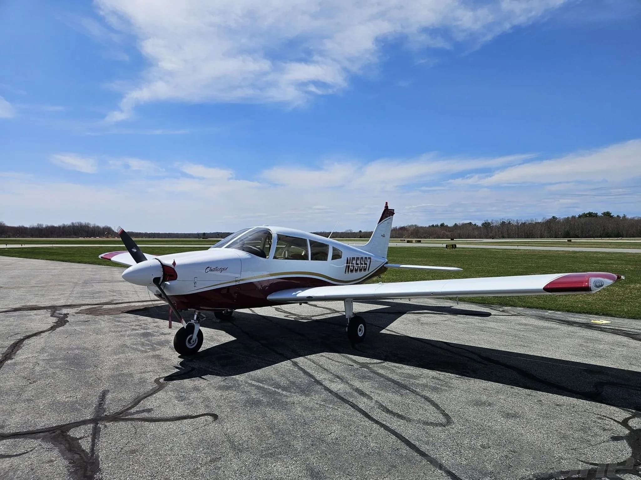 Three-quarter front view of a white and maroon Piper PA-28 Challenger aircraft with registration N55667 on an airfield.