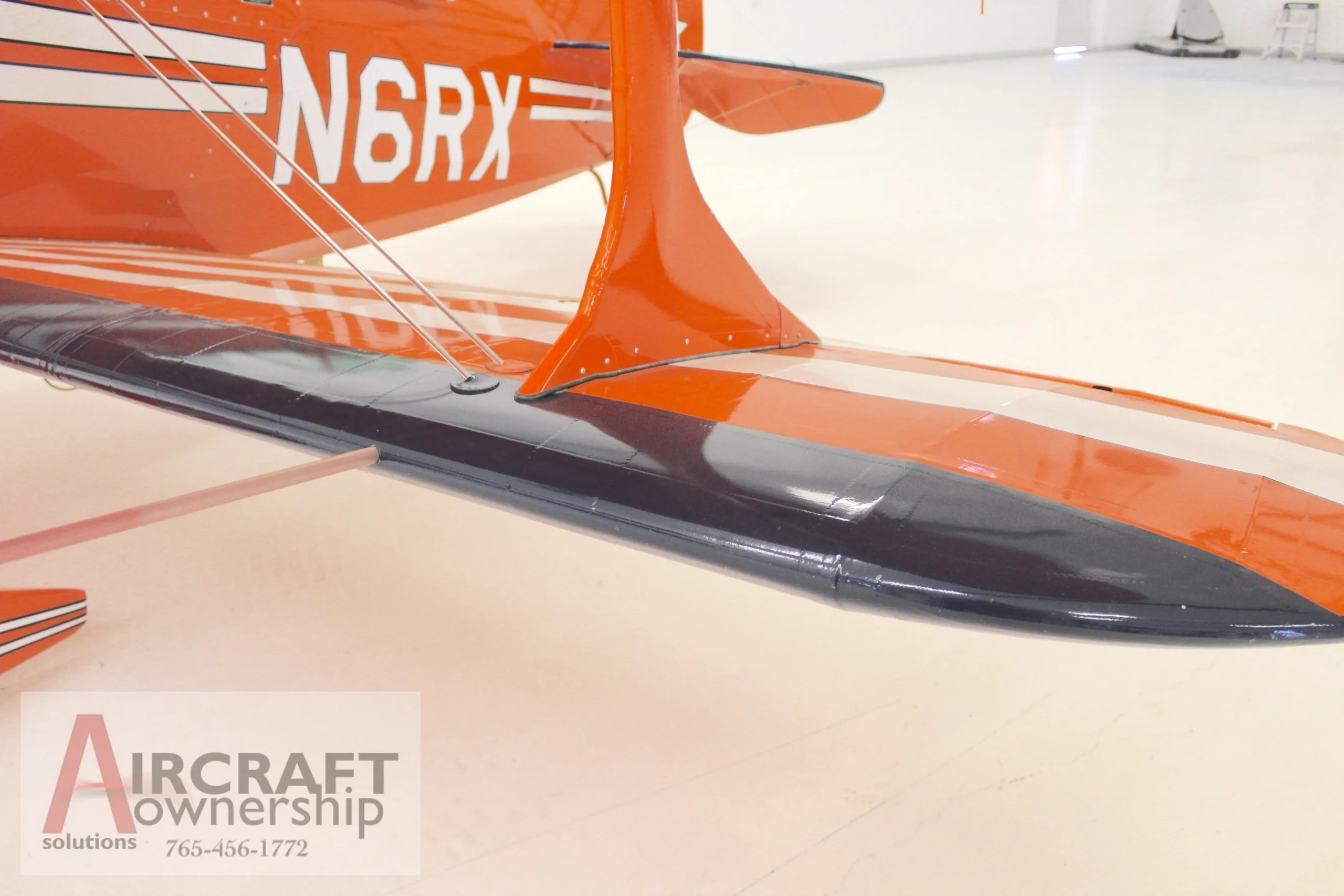 A close-up view of the lower wing and fuselage of an orange Pitts S-1T biplane, highlighting the wing strut.