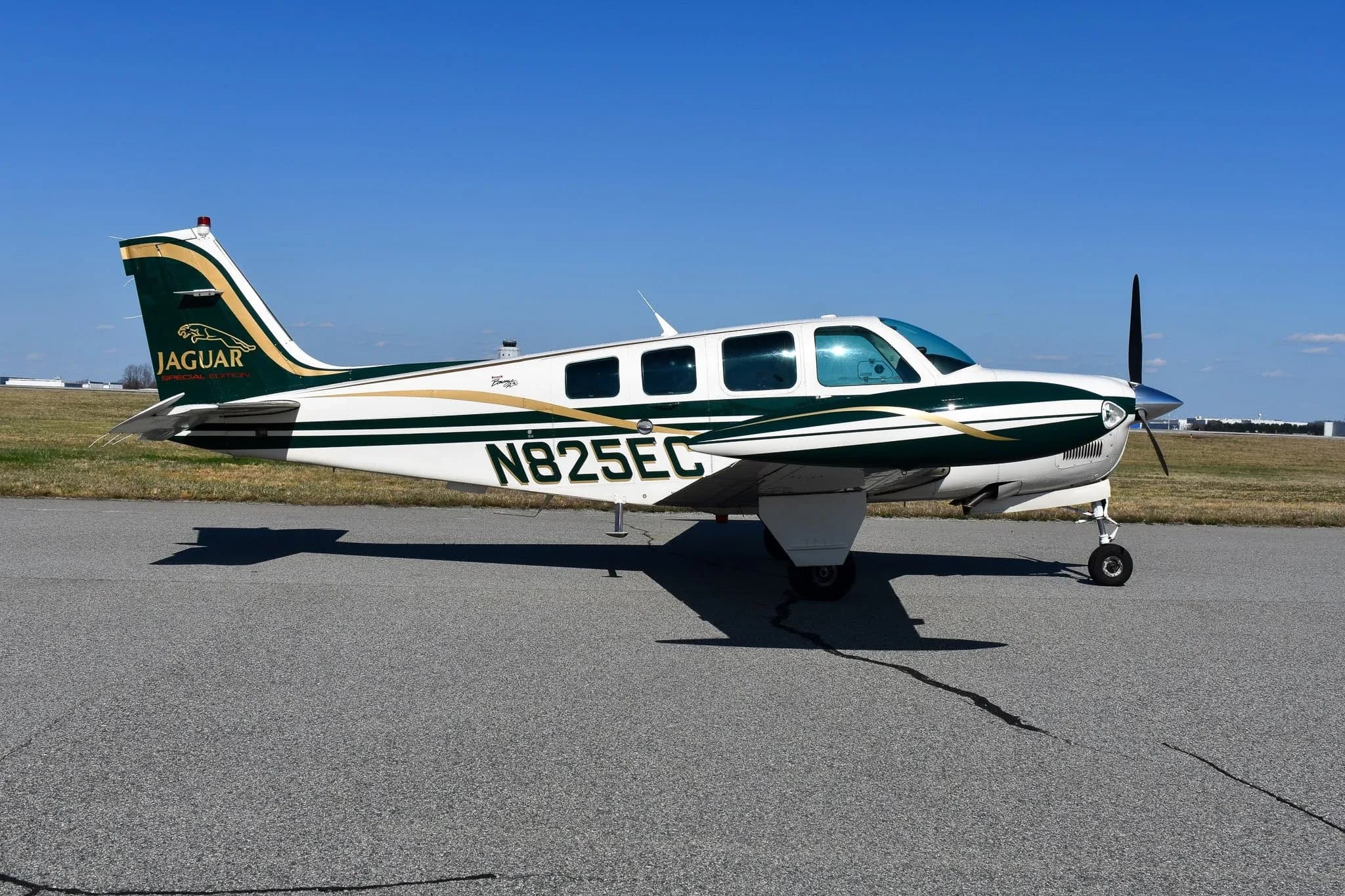 A side view of the N825EC Beechcraft Bonanza A36, painted white and dark green with gold stripes and a "Jaguar Special Edition" logo, parked on an airport tarmac.