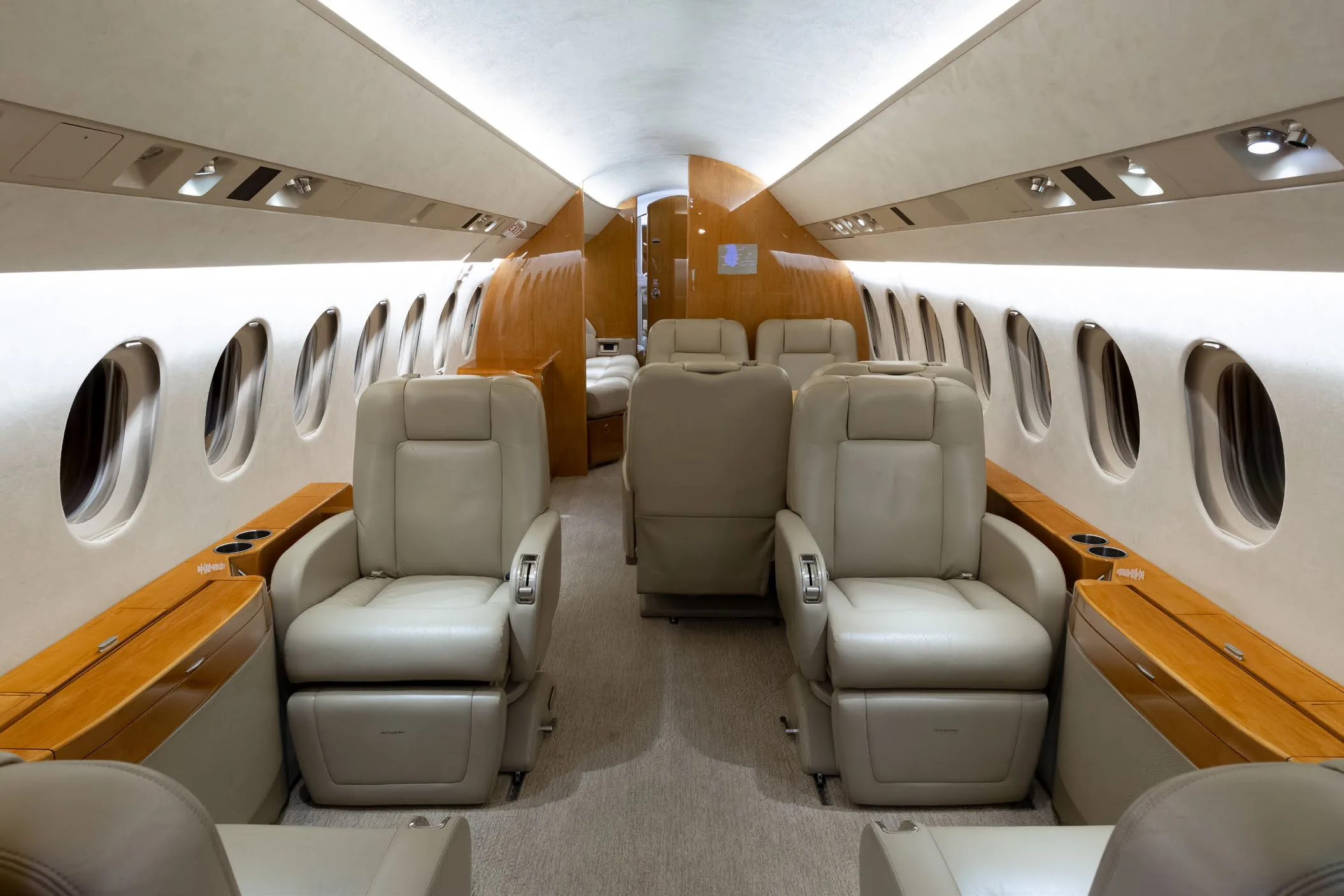 The luxurious interior cabin of a private jet, featuring light beige leather seats and polished wood accents.