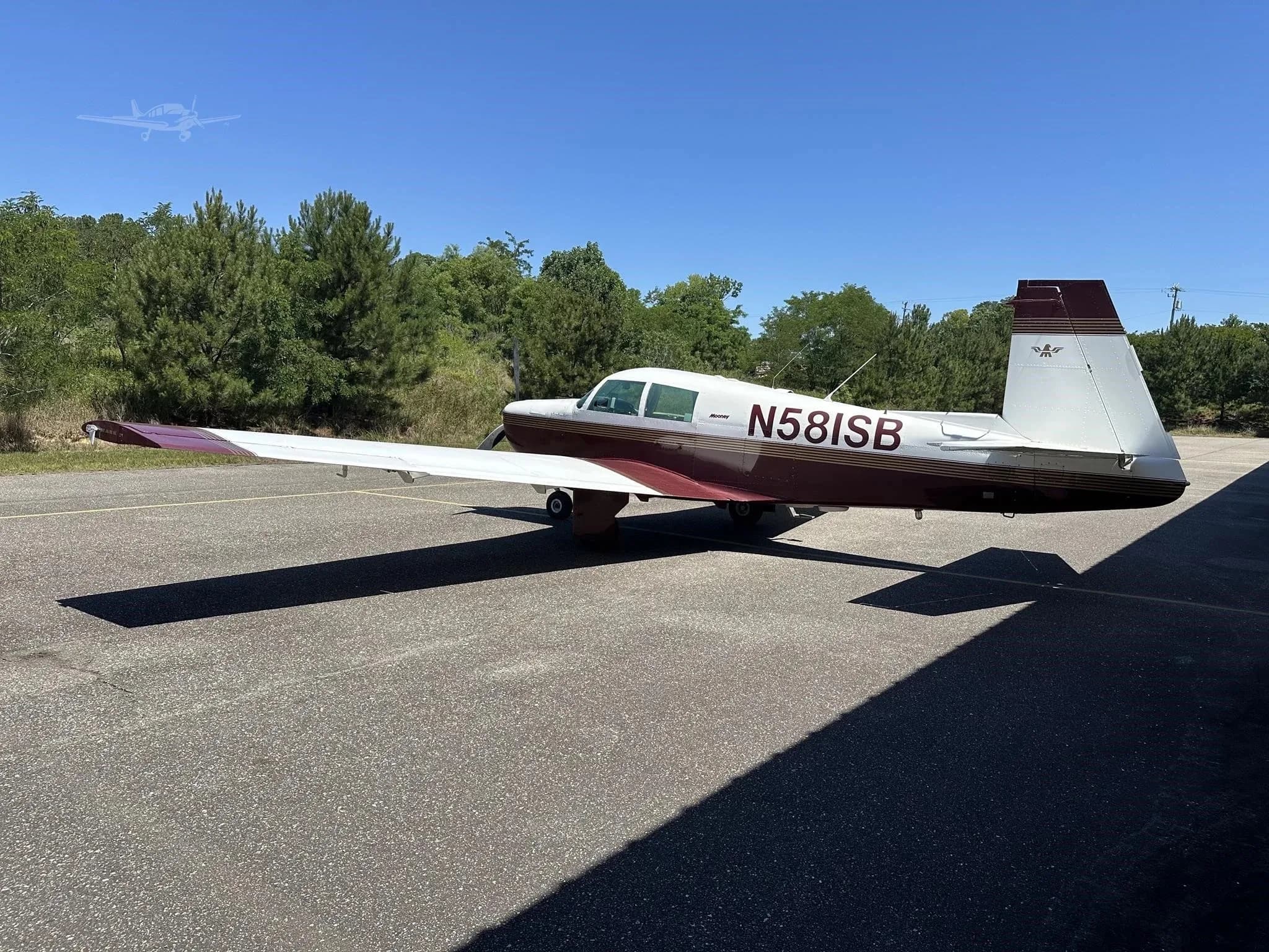A rear-side view of the white and maroon Mooney M20 Mark 21 aircraft, registration N581SB, parked on an asphalt ramp.