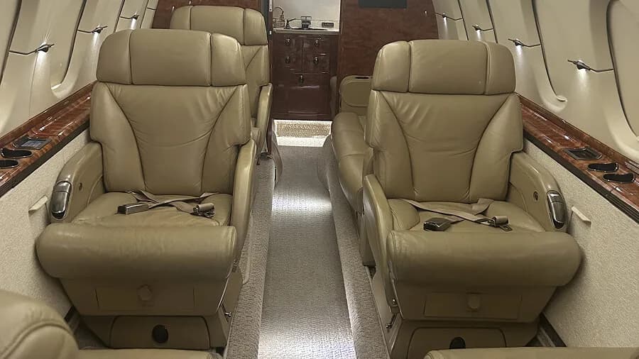 The luxurious interior cabin of a business jet with beige leather seats and wood trim.