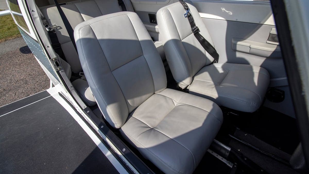 Aircraft interior featuring gray leather seats with black seatbelts.