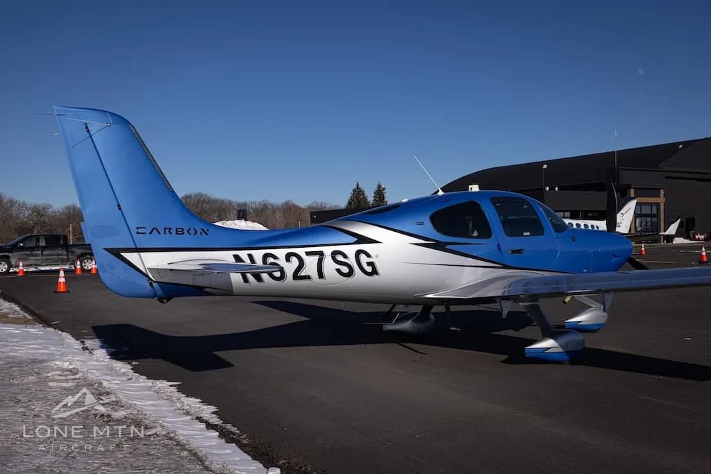 A rear-side view of the blue and silver Cirrus SR22 aircraft (N627SG) parked near a hangar.