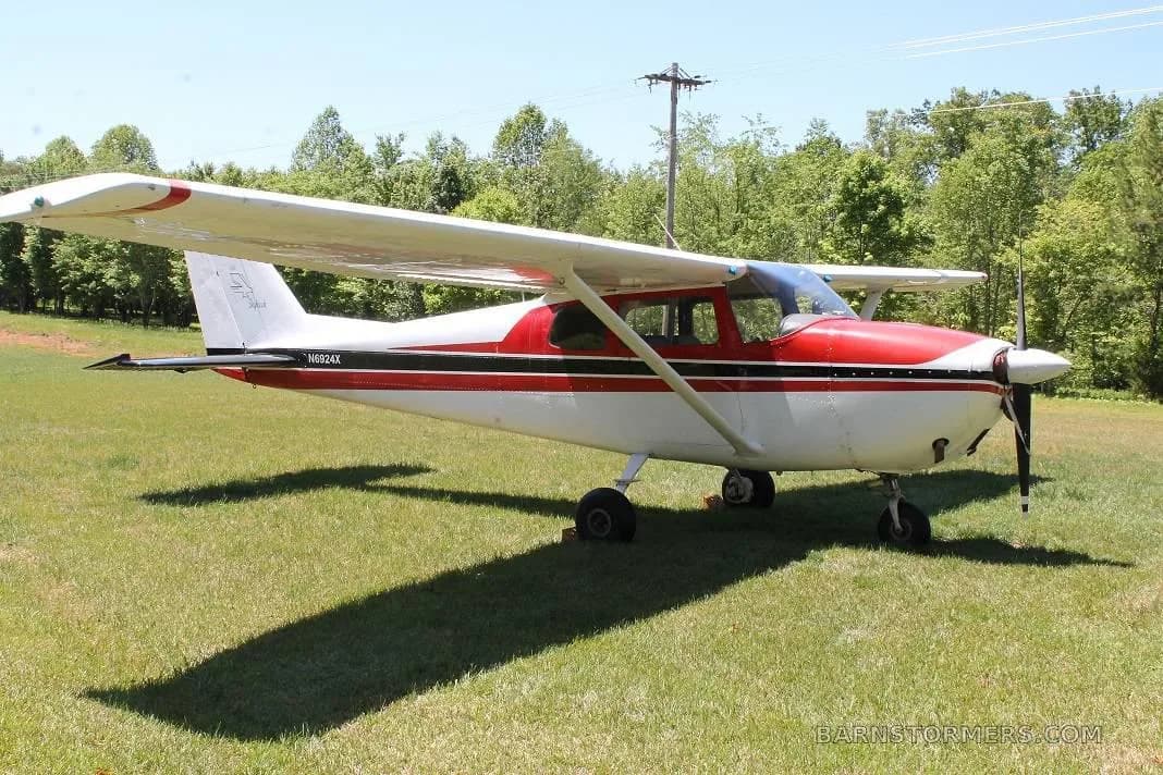 A red and white Cessna 172 with a black stripe, parked on a grassy field under a clear sky.