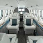 A view of a luxurious aircraft cabin with light grey and blue leather seats arranged in a club configuration.