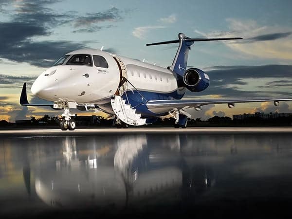 A Embraer Praetor 600 business jet on the tarmac with the door open at sunset.