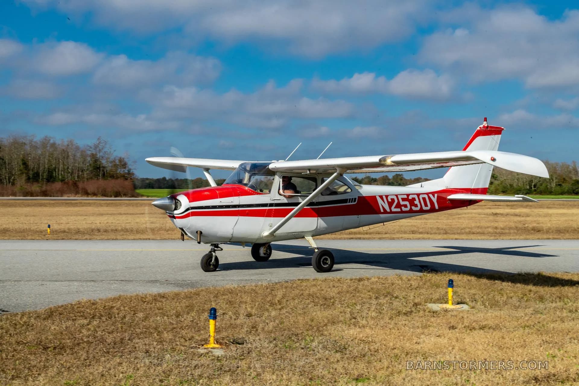 A white and red single-engine propeller aircraft, N2530Y, is taxiing on a paved surface under a blue sky.